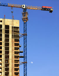 Low angle view of crane against clear blue sky