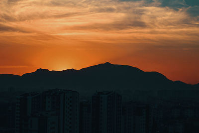 Silhouette buildings against mountains at sunset
