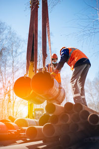 Two slingers in construction helmets and vests on street on summer day unloaded metal pipes. real