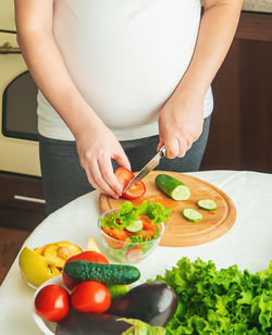 Midsection of pregnant woman cutting vegetable