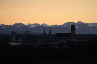 Silhouette buildings by mountains against clear sky during sunset