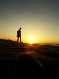 Rear view of man standing on beach against sky during sunset