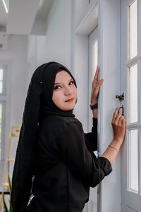 Portrait of young woman standing against wall