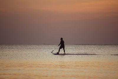 Silhouette man standing in sea against sky during sunset