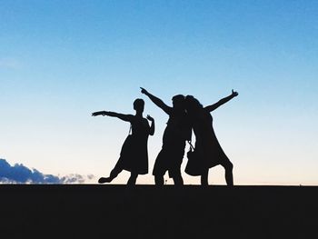 Silhouette people with hand raised against sky during sunset