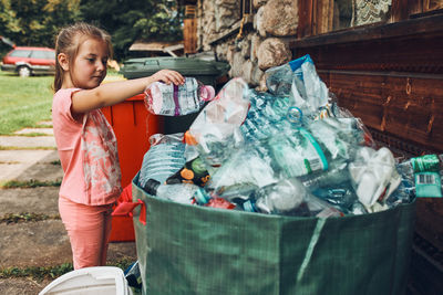 Child little girl throwing out plastic bottle to big container full of plastic waste