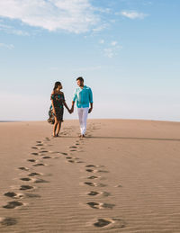 Rear view of woman walking at beach against sky