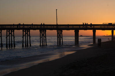 Silhouette pier on beach against clear sky at sunset