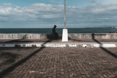 Man standing on footpath by sea against sky