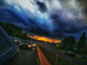 Cars on road against cloudy sky