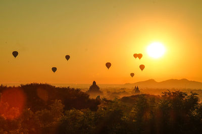 Hot air balloons flying over silhouette landscape against sky during sunset