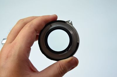 Cropped hand holding camera lens against white background