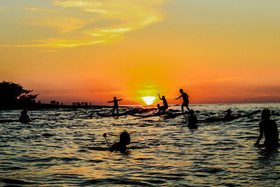 Silhouette people enjoying at beach against orange sky during sunset