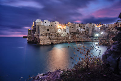 Buildings by sea against sky during sunset