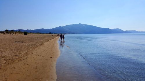 Scenic view of people walking on mountain by sea against clear sky