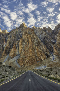 Country road by mountains against sky