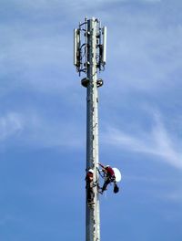 Electric utility worker on pole against blue sky