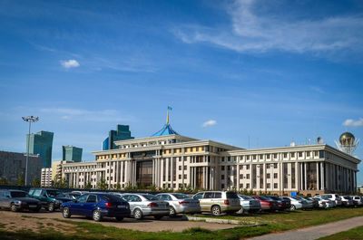 Cars on road by buildings against blue sky