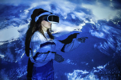 Close-up of woman wearing virtual reality standing against illuminated wall