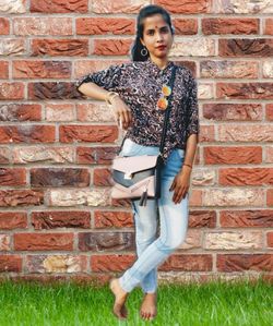 Portrait of young woman holding umbrella against brick wall