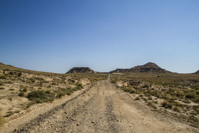 Road amidst desert against clear blue sky