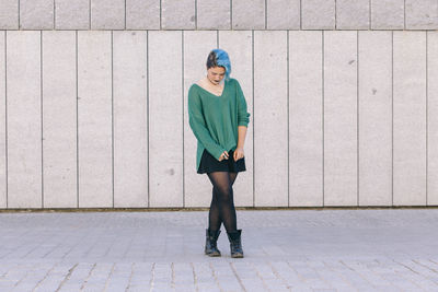 Full length portrait of a woman standing against wall