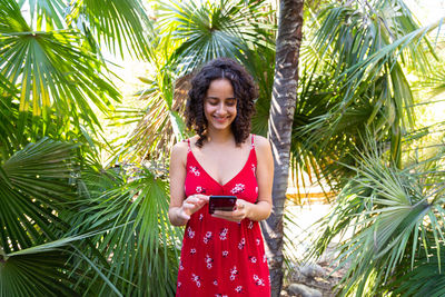 Portrait of young woman standing against palm tree