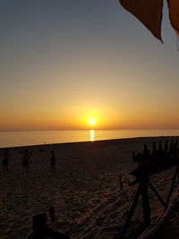 Silhouette people on beach against clear sky during sunset