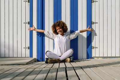 Portrait of cheerful woman with roller skates sitting by wall