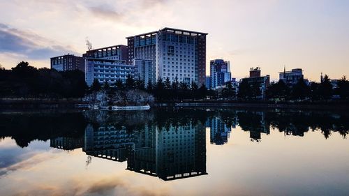 Reflection of buildings in lake against sky during sunset