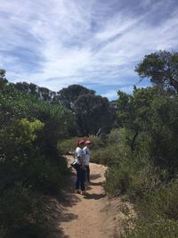 People walking on footpath in forest against sky