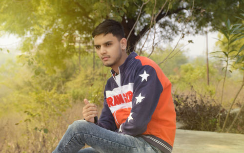 Young man looking away while sitting on tree