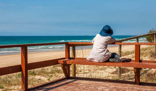 Rear view of woman sitting on railing against sea