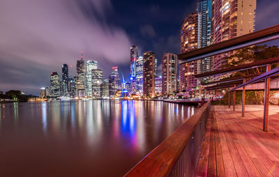 Illuminated buildings by river against sky at night