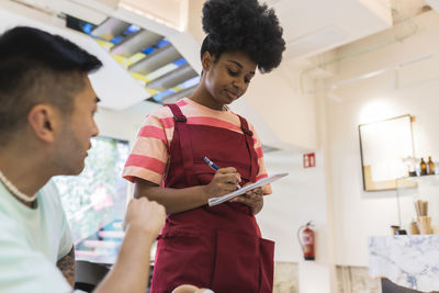 Young waitress taking order from customer in cafe