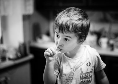 Cute boy sucking thumb while standing at home