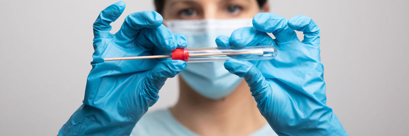 Close-up of doctor wearing mask holding test tube against gray background