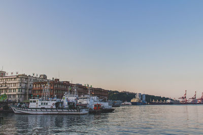 Boat moored in river by buildings against clear sky during sunset