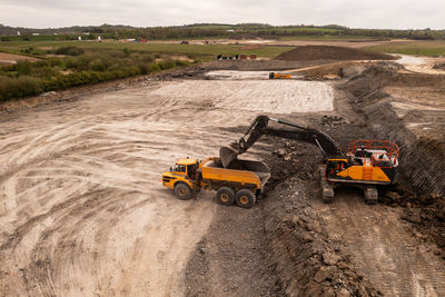 Aerial view of mechanical digger with grab loading a dumper truck with soil on a  construction site