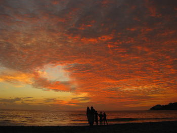 Silhouette people on beach against orange sky