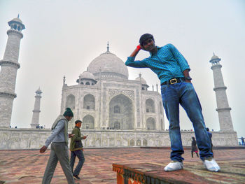 Optical illusion of young man leaning on taj mahal