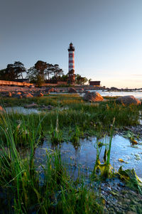 Lighthouse by sea against sky during sunset