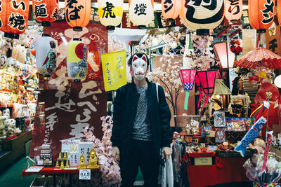 Man wearing maneki neko mask against market stall