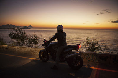 Rear view of man riding motorcycle by sea during sunset