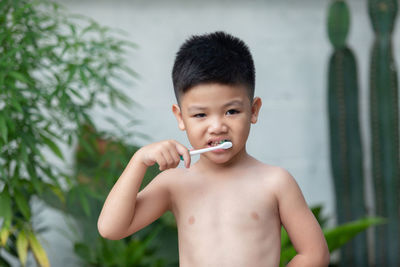 Portrait of shirtless boy brushing teeth standing outdoors