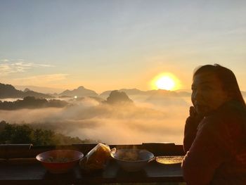 Woman with food on table siting against sky during sunset