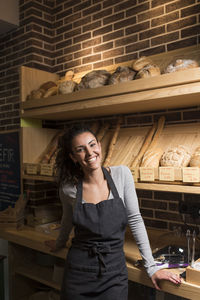 Smiling young owner standing against baked food rack in illuminated bakery