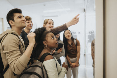 Multiracial male and female students checking result on bulletin board in university