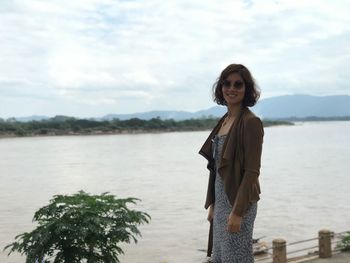 Portrait of smiling woman standing by lake against sky