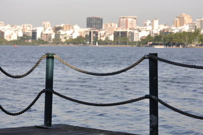 Close-up of metal fence by river against buildings in city